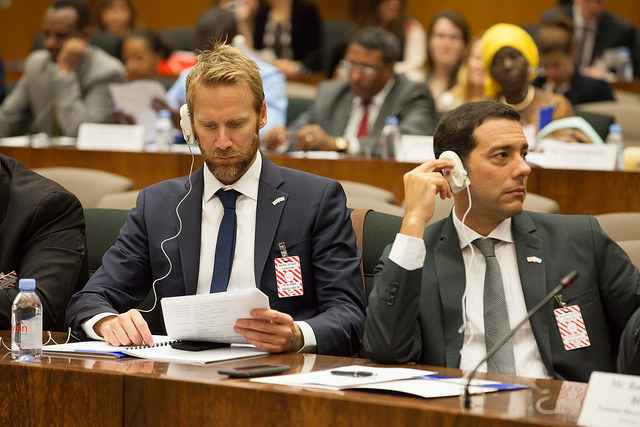 Two men wearing headphones surrounded by others in a large meeting room