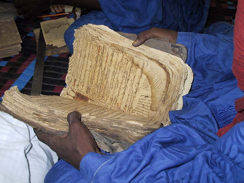 Close up of a very large and old book being held opened, the pages are wrinkled and tainted yellow