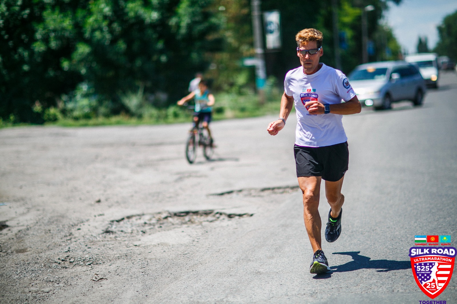 Man running on street with cars and young biker blurred in background