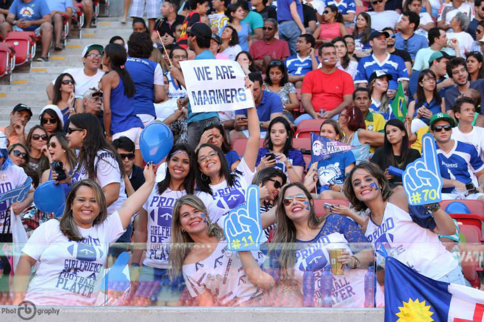 Fans in stadium look excited and hold signs cheering on the Mariner team