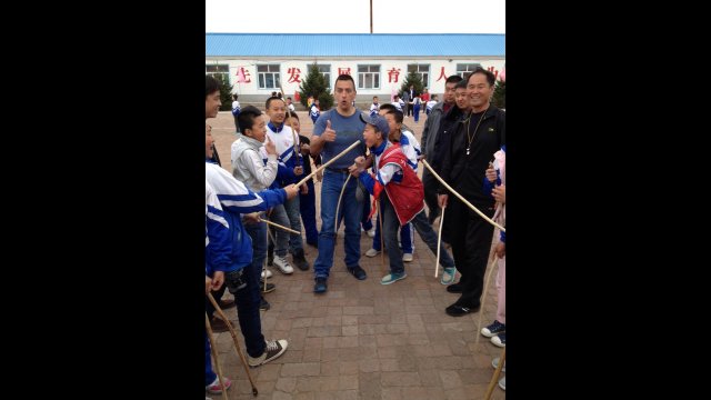 An American participant teaches Native American games to a group of Chinese boys during an outdoor activity.