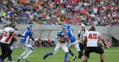 Football player running between opposing players with the football